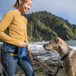 Load image into Gallery viewer, P.L.A.Y.'s Explorer Pack in Waterfall Blue on a dog mom giving her dog a treat out of the treat pouch on beach with dog staring intently
