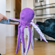 Load image into Gallery viewer, Big black dog tugging with Play’s Ocean Buddies Opal the Octopus toy held by a person indoors.
