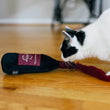 Load image into Gallery viewer, Cat creeping up to sniff the P.L.A.Y. Feline Frenzy Catbernet Sauv Kicker Toy on a wooden floor
