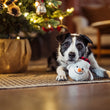Load image into Gallery viewer, A black-and-white dog lies on a woven rug next to a potted Christmas tree, holding its head over a Play Merry Minis Brrr-ian snowman head toy.
