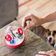 Load image into Gallery viewer, P.L.A.Y. Holiday Wobble Ball 2.0 - dog parent loading treats into cloud-shaped opening while dog watches from below the kitchen counter

