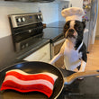 Load image into Gallery viewer, Clive &amp; Bacon x P.L.A.Y. Crispy Bacon Toy - in pan on stove with black and white dog wearing a chef's coat and hat behind it
